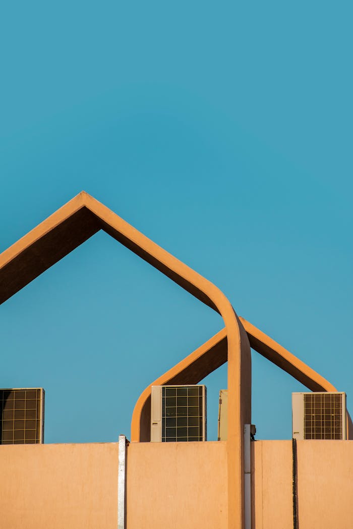 about-01 Modern architectural design featuring geometric roof structure and air conditioning units against a clear blue sky.